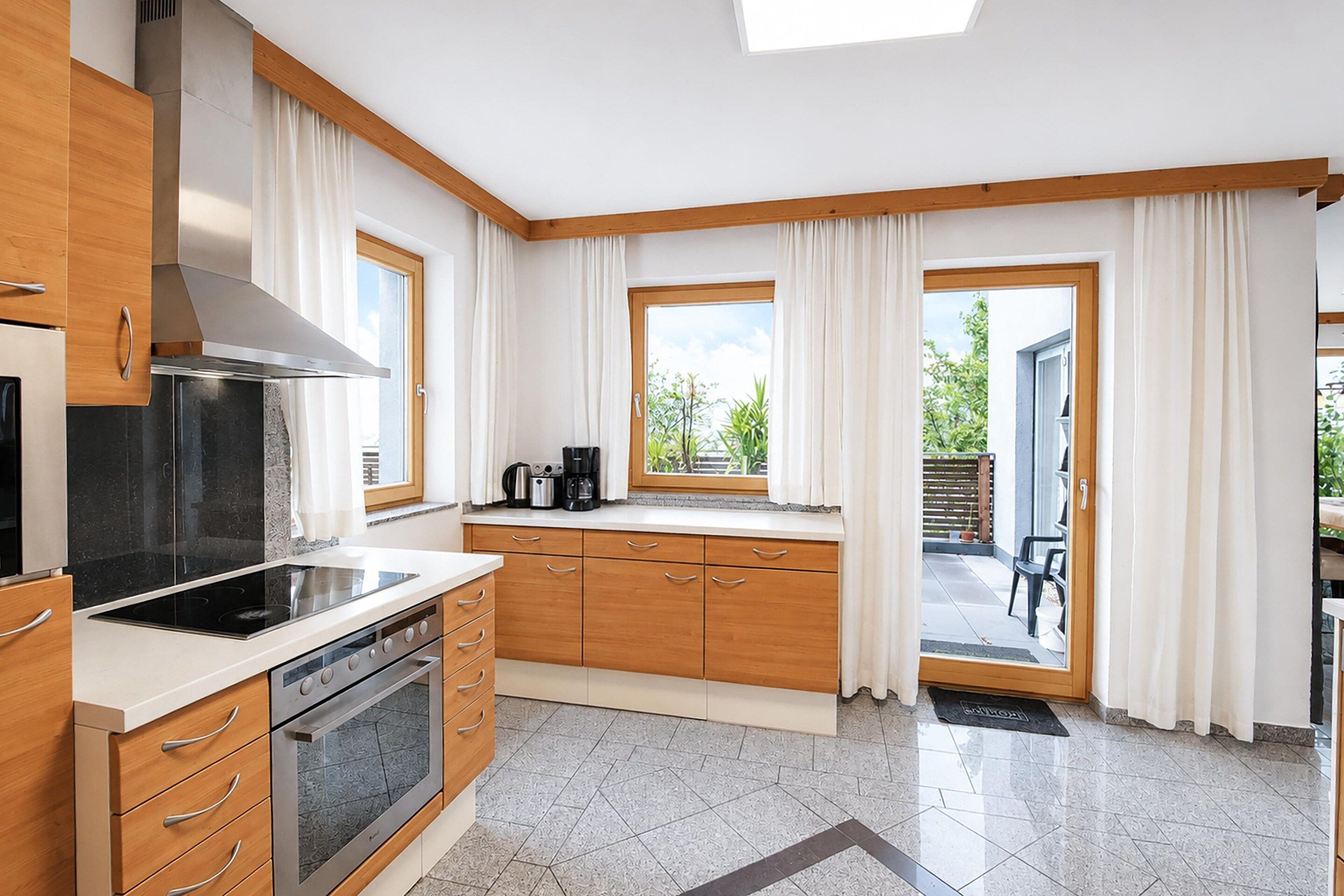 Une cuisine moderne avec des meubles en bois, un four encastré et une fenêtre donnant sur un jardin.