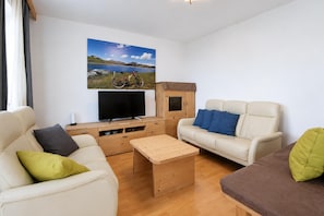A modern living room with a sofa, a coffee table, a TV, and a painting of a mountain landscape. - Apartment in Aschau Near Ski Lift Kaltenbach (Aschau Im Zillertal)