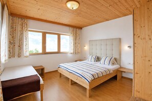 A bedroom with a wooden bed, a bedside table, a nightstand, a window with curtains, and a ceiling light. - Apartment in Aschau Near Ski Lift Kaltenbach (Aschau Im Zillertal)
