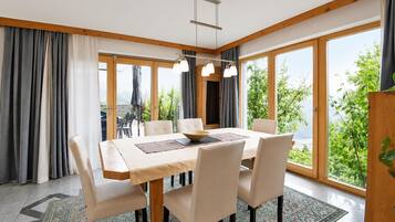 A dining area with a table set for six, large windows, and a view of greenery.