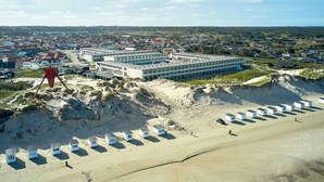 A coastal hotel with multiple buildings, a sandy beach with beach huts, and a forested background. - 6 Person Holiday Park Home in Blokhus (Blokhus)