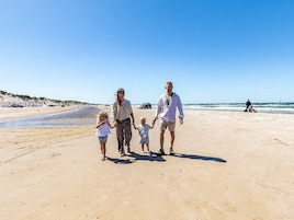 Una familia caminando sobre una playa arenosa con cielo despejado.