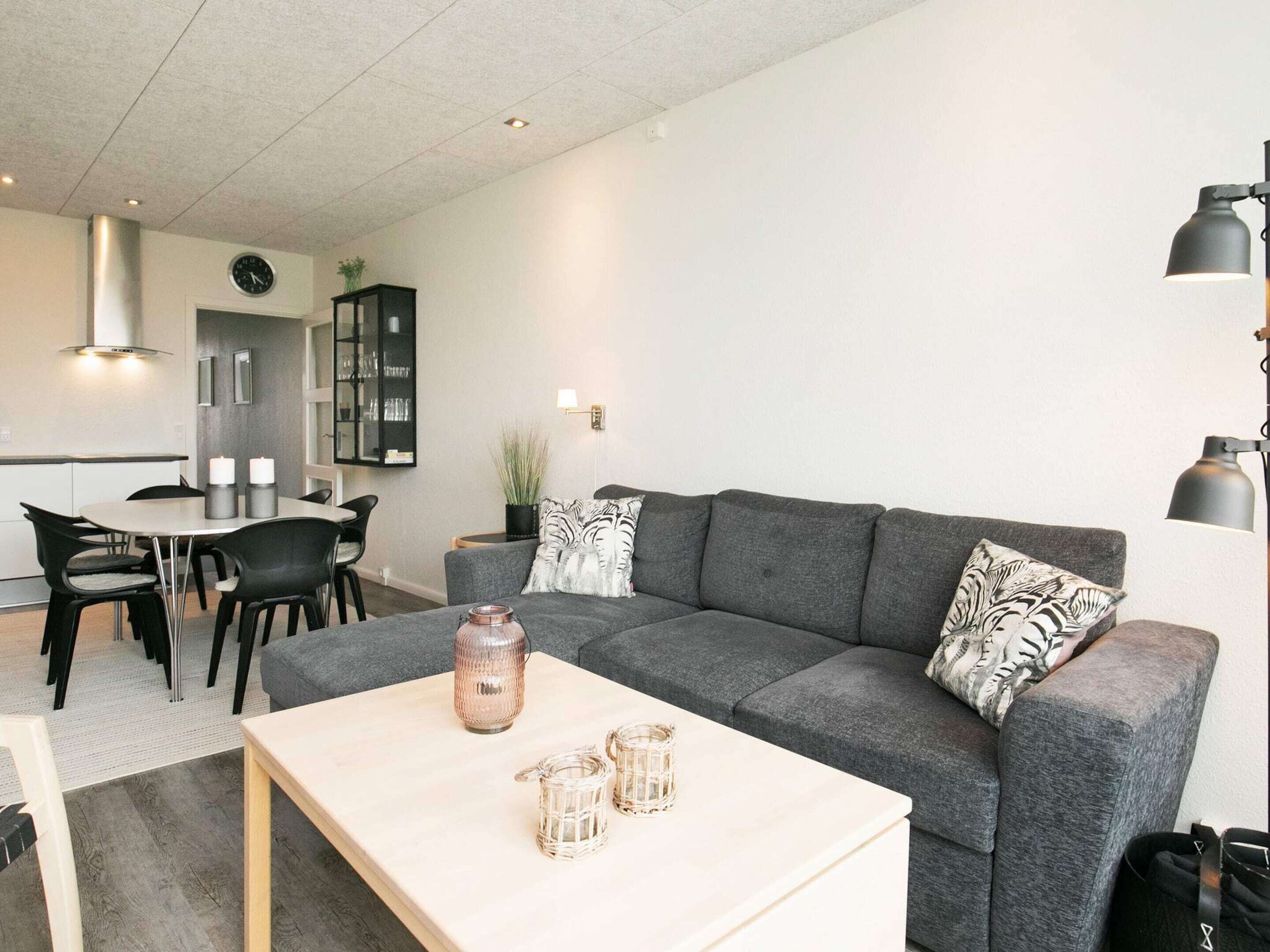 Una sala de estar moderna con un sofá gris, una mesa de centro y una zona de comedor con mesa y sillas.