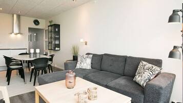 Una sala de estar moderna con un sofá gris, una mesa de centro y una zona de comedor con mesa y sillas.