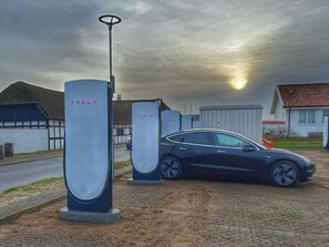 Een Tesla elektrische auto laadstation met een auto in de buurt.