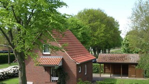 A brick house with a red-tiled roof, a covered porch, and a garden area. - Holiday Home Osteland (Estorf)
