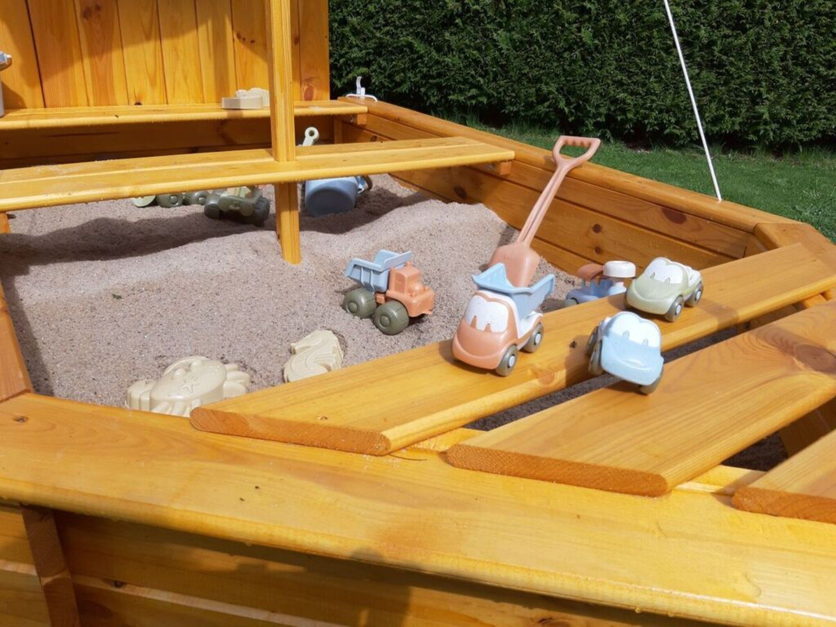 A wooden play area with a sandbox, toy vehicles, and a shovel.