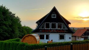 A house with a triangular roof, a wooden barrel, and a white fence. - Fingerhut Comfortable Holiday Residence (Braunlage)