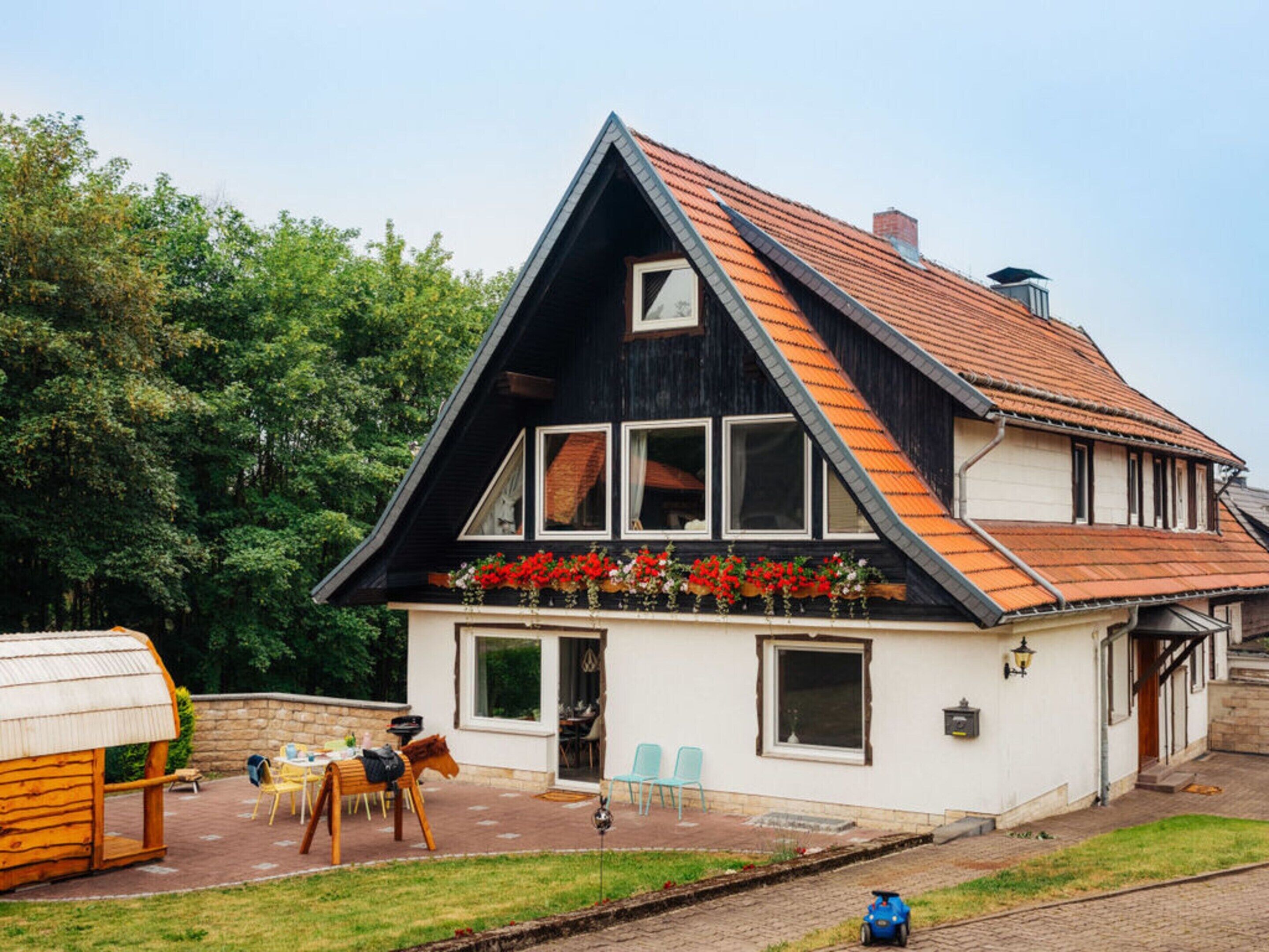 Une maison à deux étages, dotée d’un toit à forte pente, d’un balcon orné de jardinières et d’un petit espace extérieur aménagé avec des chaises et une table.