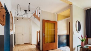 A spacious room with a wooden floor, a staircase, a wooden door with glass panels, and a small table with a vase of flowers. - Fingerhut Comfortable Holiday Residence (Braunlage)
