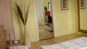 A hotel room with two beds, a bedside table with a lamp, a vase with plants, and a mirror reflecting a dining area. - Holiday Apartment Casabrema (Bremen)