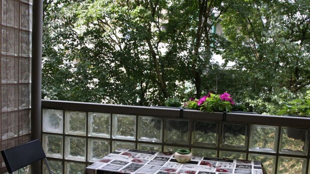 A balcony with a table covered in a newspaper collage, surrounded by chairs, and a potted plant with pink flowers. - Holiday Apartment Casabrema (Bremen)