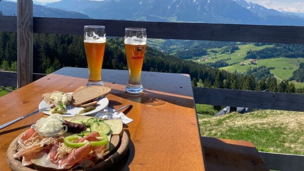 A table with a meal and two glasses of beer, overlooking a mountainous landscape. - Waterval in het Huis Boshoek (Aschau im Chiemgau)