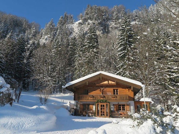 A wooden cabin with a balcony, surrounded by snow-covered trees.