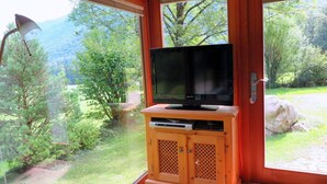 A wooden entertainment unit with a television in a room with large windows. - Waterval in het Huis Boshoek (Aschau im Chiemgau)