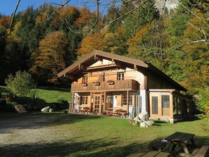 A wooden cabin with a balcony, surrounded by a grassy area and trees.