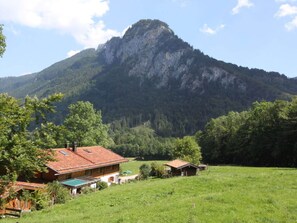 A mountain with a prominent peak, surrounded by lush greenery and a few buildings with red-tiled roofs.
