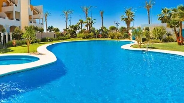 Una piscina de diseño curvo, rodeada de palmeras y un edificio con balcones.