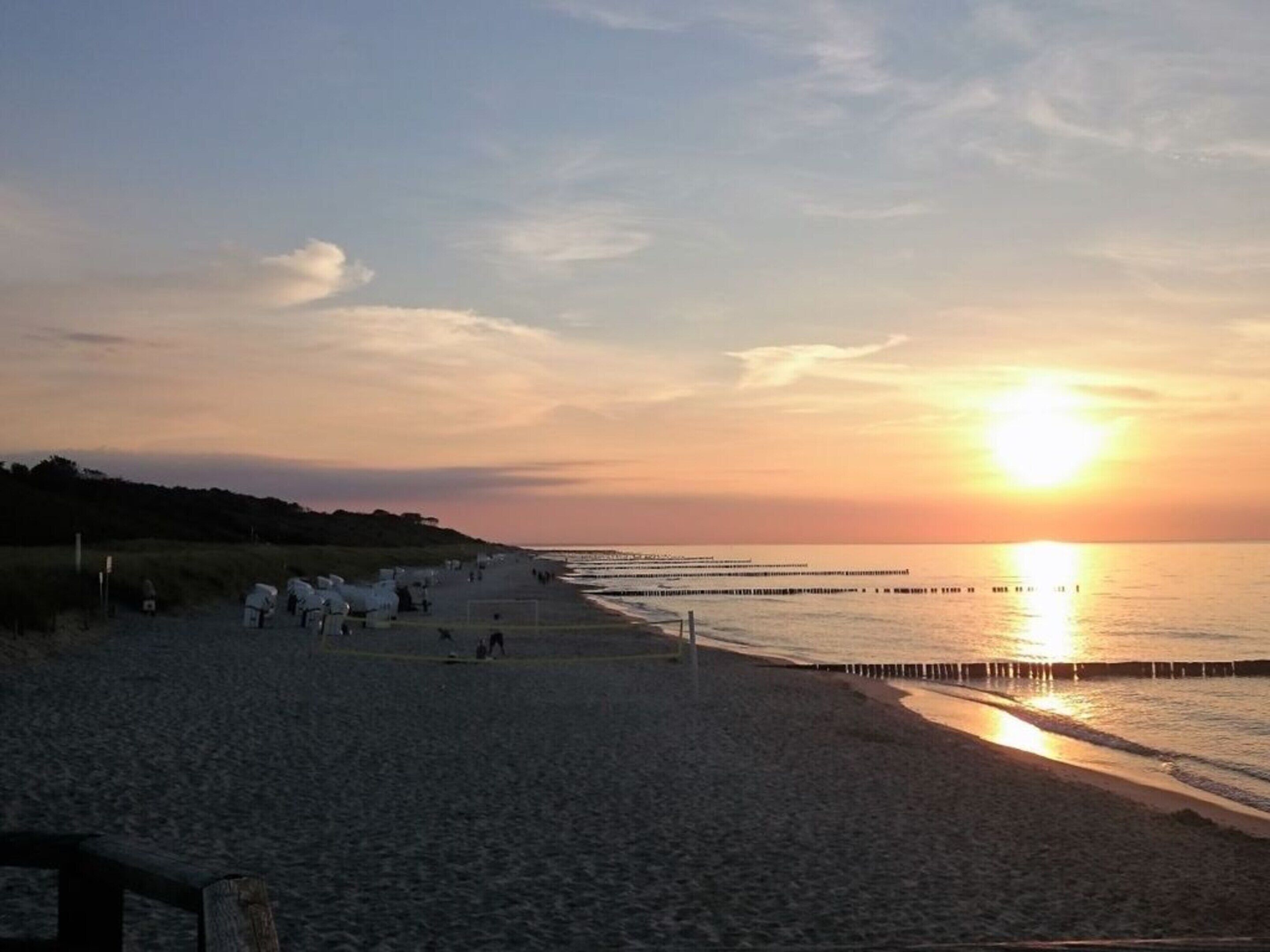 A beach with a sunset, calm sea, and a pier extending into the water.