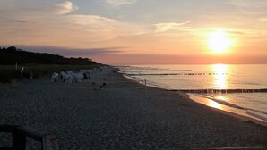 Uma praia com um pôr do sol, mar calmo e um píer que se estende sobre a água.