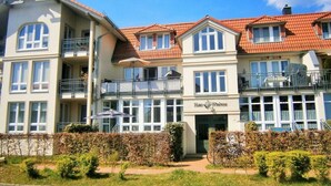 Um hotel com vários andares, varandas, entrada central e um jardim bem cuidado.