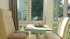 Quarto com sofá, mesa, cadeiras, um lustre e janelas amplas.