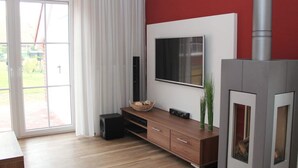 A modern living room with a large TV, a fireplace, and a sliding glass door leading to an outdoor area.