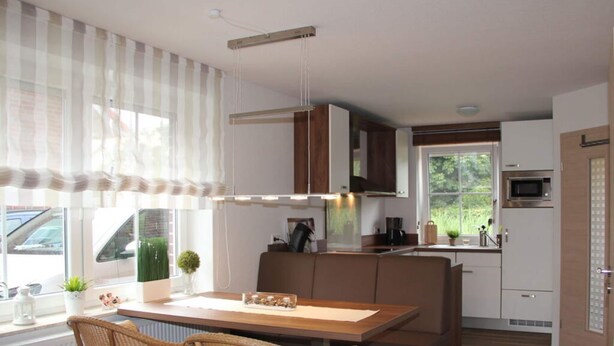 A modern kitchen with a wooden table and chairs, a microwave, and a window with curtains.