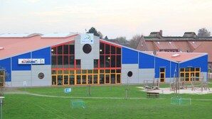 A modern building with a blue and grey facade, large windows, and a red roof.