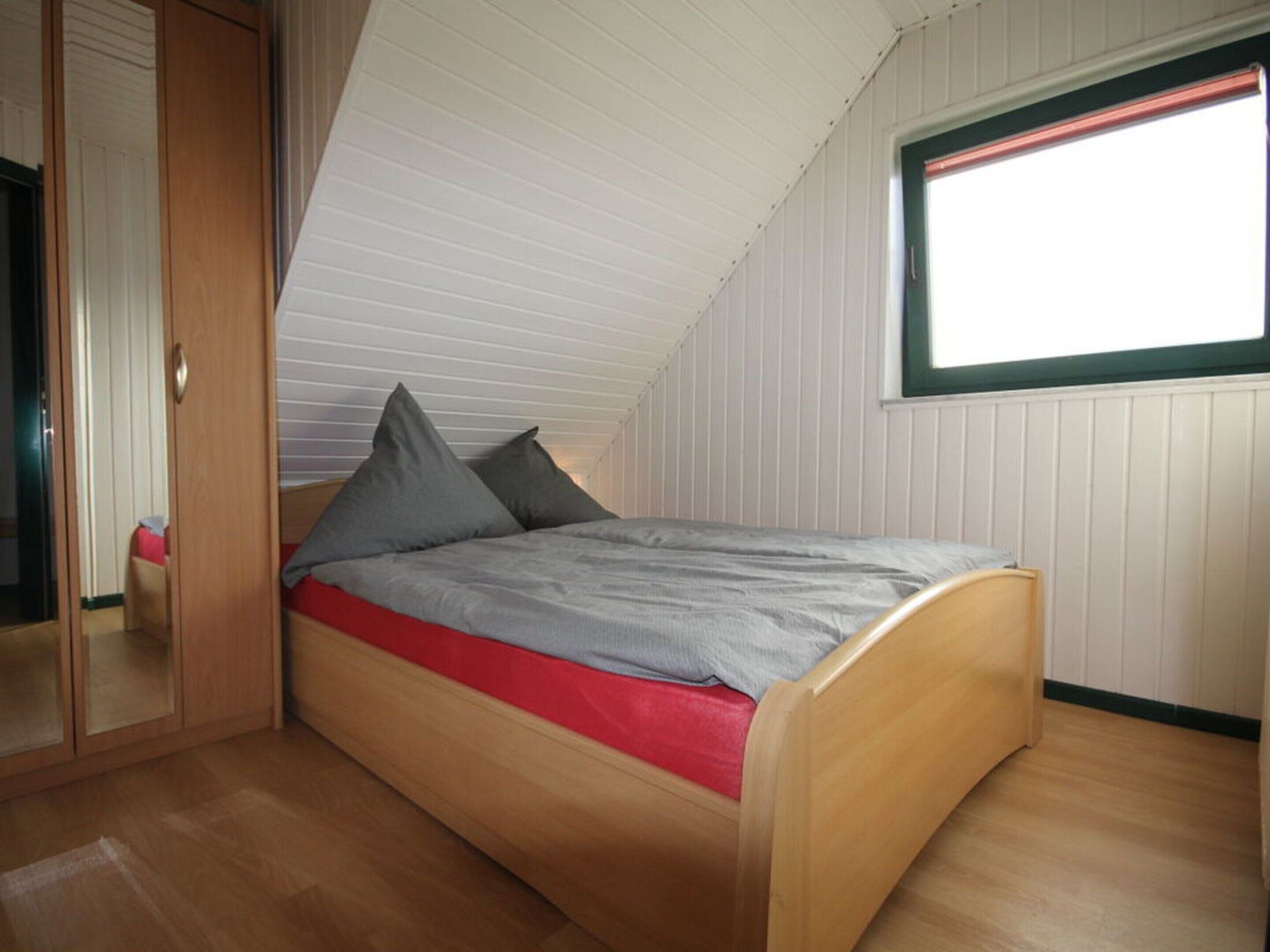 A single bed with a red mattress and grey bedding in a room with wooden flooring and white walls.