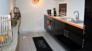 A modern kitchen with a black and orange color scheme, featuring a built-in oven, a sink, and a coffee machine. - Living Lust 3 in Malchow (Malchow)