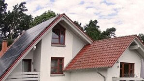 A two-story white house with a red-tiled roof, a garden with various plants and flowers, and a patio area with outdoor furniture. - Living Lust 3 in Malchow (Malchow)