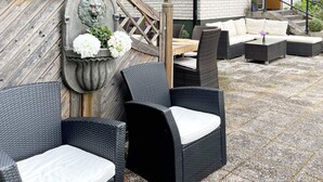 A patio with wicker furniture, a stone lion sculpture, and a white brick building in the background. - 4 Star Holiday Home in Olofstrom (Olofström)