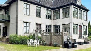 A two-story building with a brick facade, multiple windows, and a covered outdoor seating area with chairs and tables. - 4 Star Holiday Home in Olofstrom (Olofström)