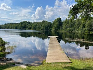 Un lago tranquilo con un muelle de madera que se adentra en el agua, rodeado de árboles frondosos.