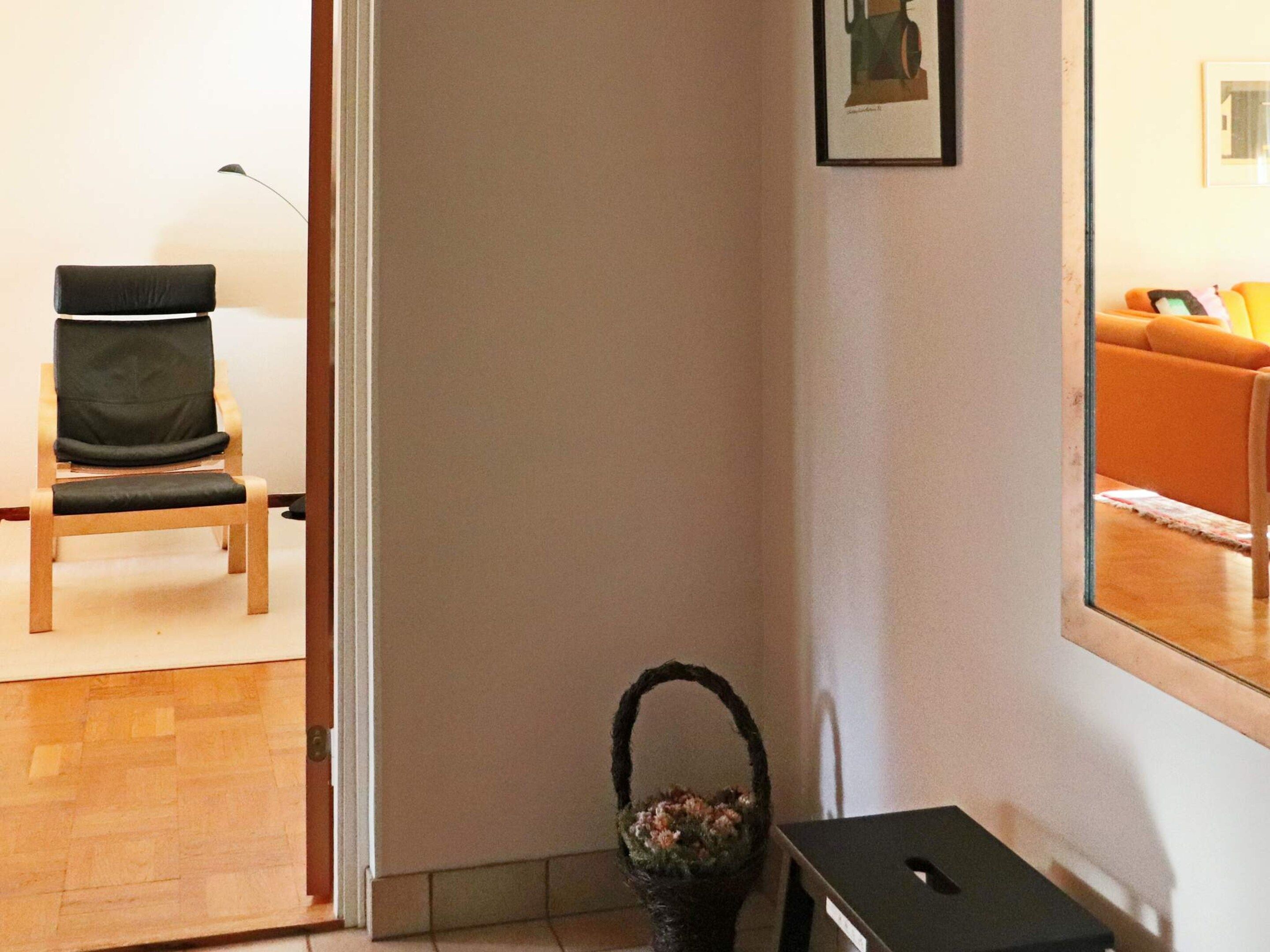 A room with a wooden chair, a small table, a basket with flowers, and a framed picture on the wall.