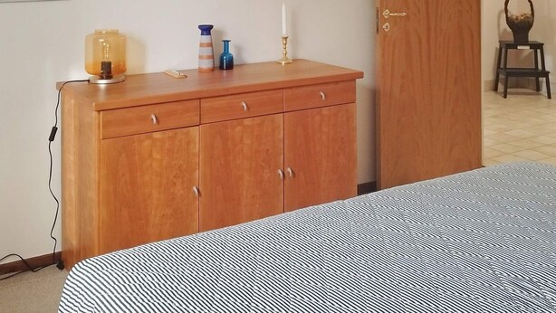 A bedroom with a bed, a wooden dresser, and artwork on the walls. - 4 Person Holiday Home in Hyltebruk (Hyltebruk)