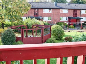 A residential area with a red wooden deck, a brick house with a tiled roof, and a garden with various shrubs and trees. - 4 Person Holiday Home in Hyltebruk-by Traum (Hyltebruk)