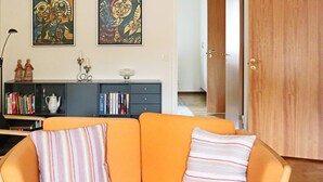 A living room with an orange sofa, two pillows, a bookshelf, and two abstract paintings on the wall. - 4 Person Holiday Home in Hyltebruk (Hyltebruk)