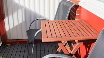 A patio with a wooden table and two chairs, a red brick wall, and a white window.