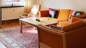 A living room with a sofa, armchairs, a coffee table, a lamp, and a window with curtains.