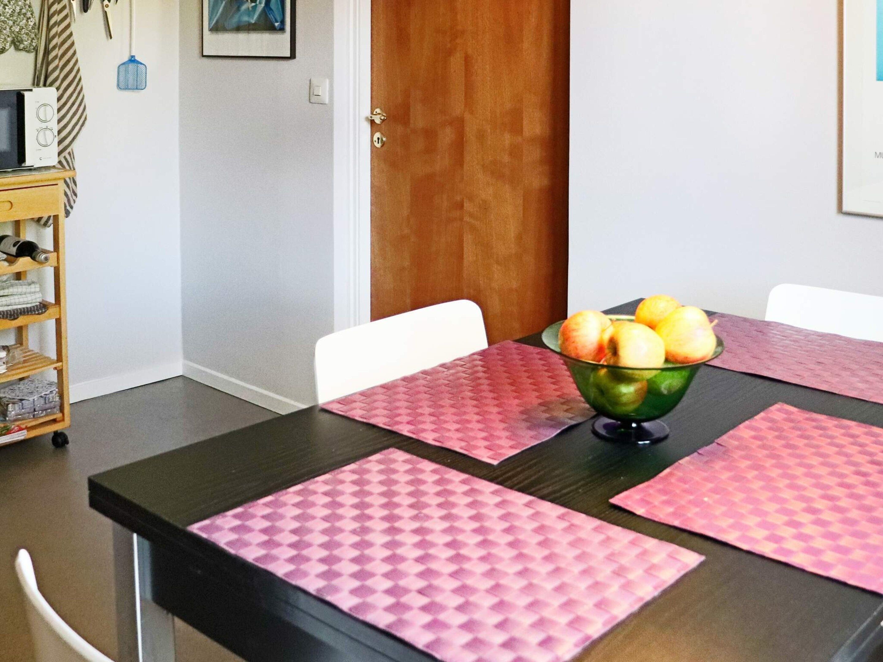 Uma mesa de jantar com jogos americanos cor-de-rosa e uma tigela de frutas.