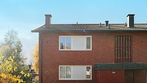 A two-story brick building with a tiled roof, two windows with white shutters, and a red gate. - 4 Person Holiday Home in Hyltebruk (Hyltebruk)