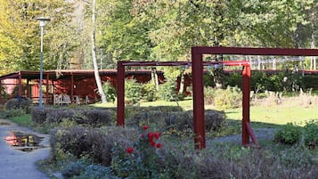 A garden pathway with a red metal structure, surrounded by greenery and a red building in the background.