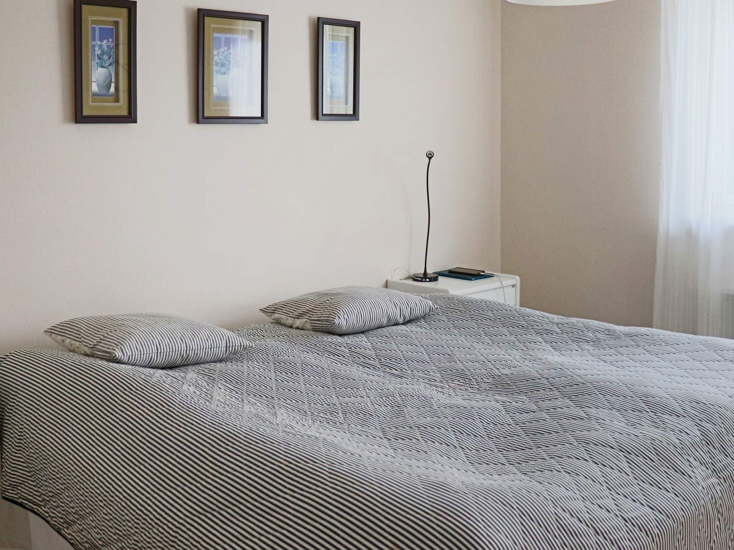 A bed with a striped bedspread, two pillows, and a bedside table with a lamp and a book.