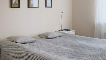 A bed with a striped bedspread, two pillows, and a bedside table with a lamp and a book.