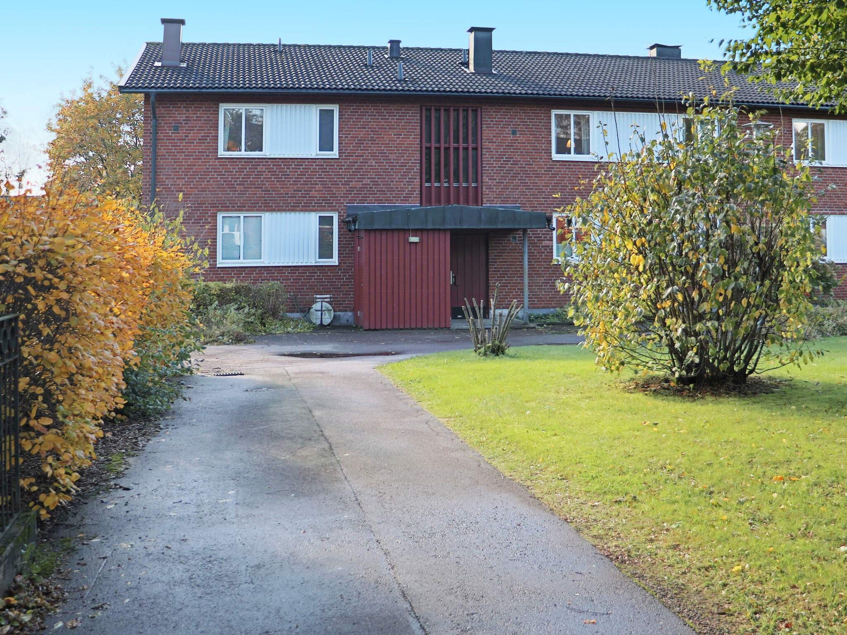 A two-story brick house with a red garage door, a small garden, and a paved driveway.
