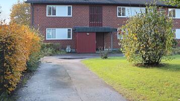 A two-story brick house with a red garage door, a small garden, and a paved driveway.