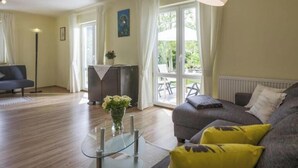 A spacious living room with a sofa, a coffee table, and a floor lamp. There is a dining table with chairs and a window with curtains. - Kaiserblick Comfortable Holiday Residence (Oberaudorf)