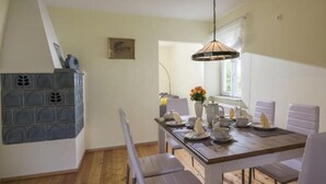 A dining area with a wooden table set for four, white chairs, and a hanging light fixture. - Kaiserblick Comfortable Holiday Residence (Oberaudorf)